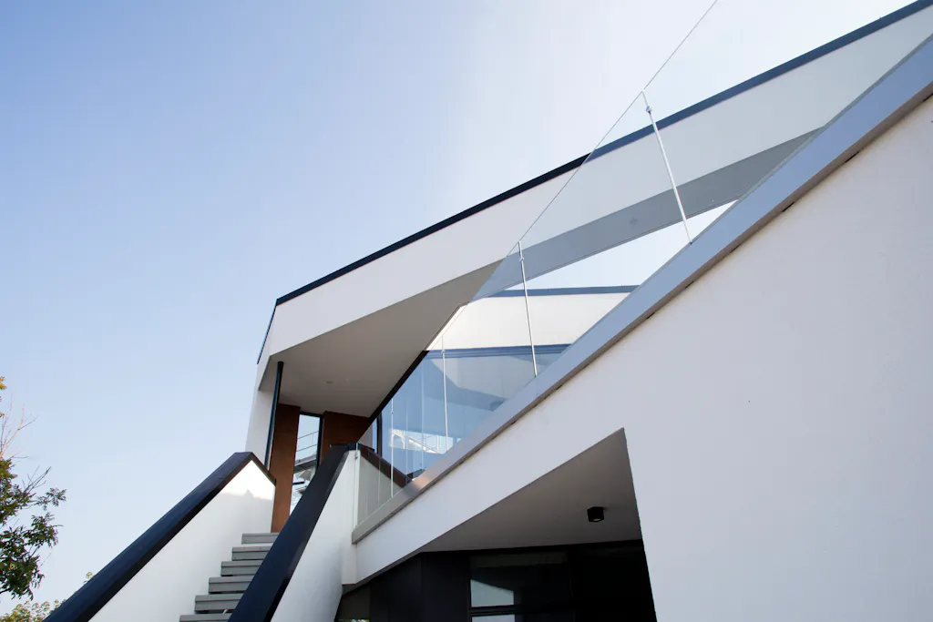 Detalj av moderne bolig med utvendig trapp, glassrekkverk og overdekket terrasse.